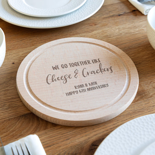 Wooden cheese board with engraved personalised text on a wooden table.