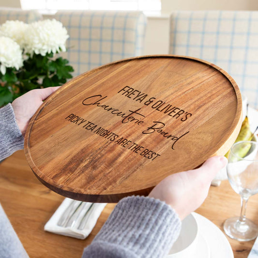 Wooden charcuterie board with engraved text held by a person in a home setting.