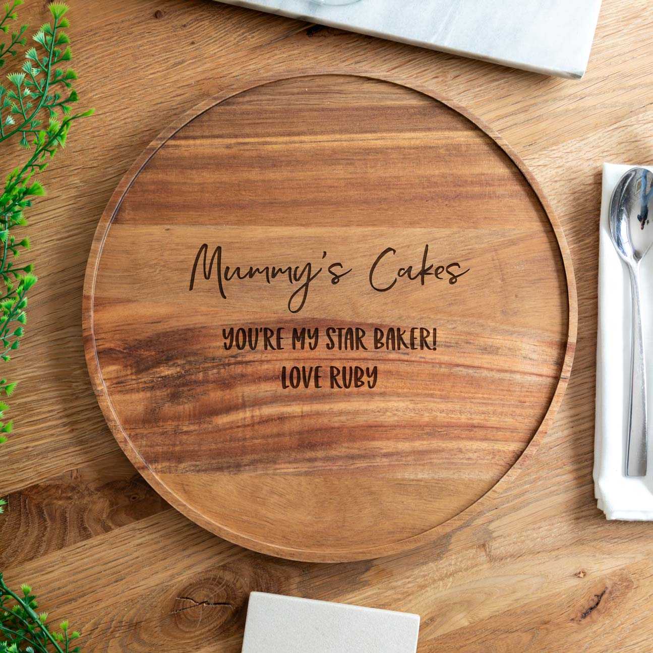 Wooden round cake board board with engraved message on a wooden surface.