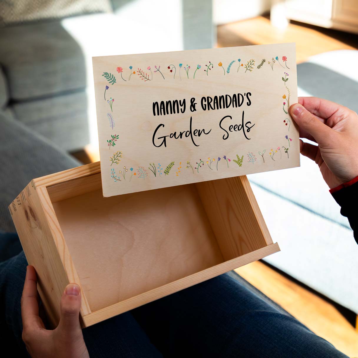 Wooden seed box printed with 'Nanny & Grandad's Garden Seeds' on the lid with a wildflower design, held by a person.