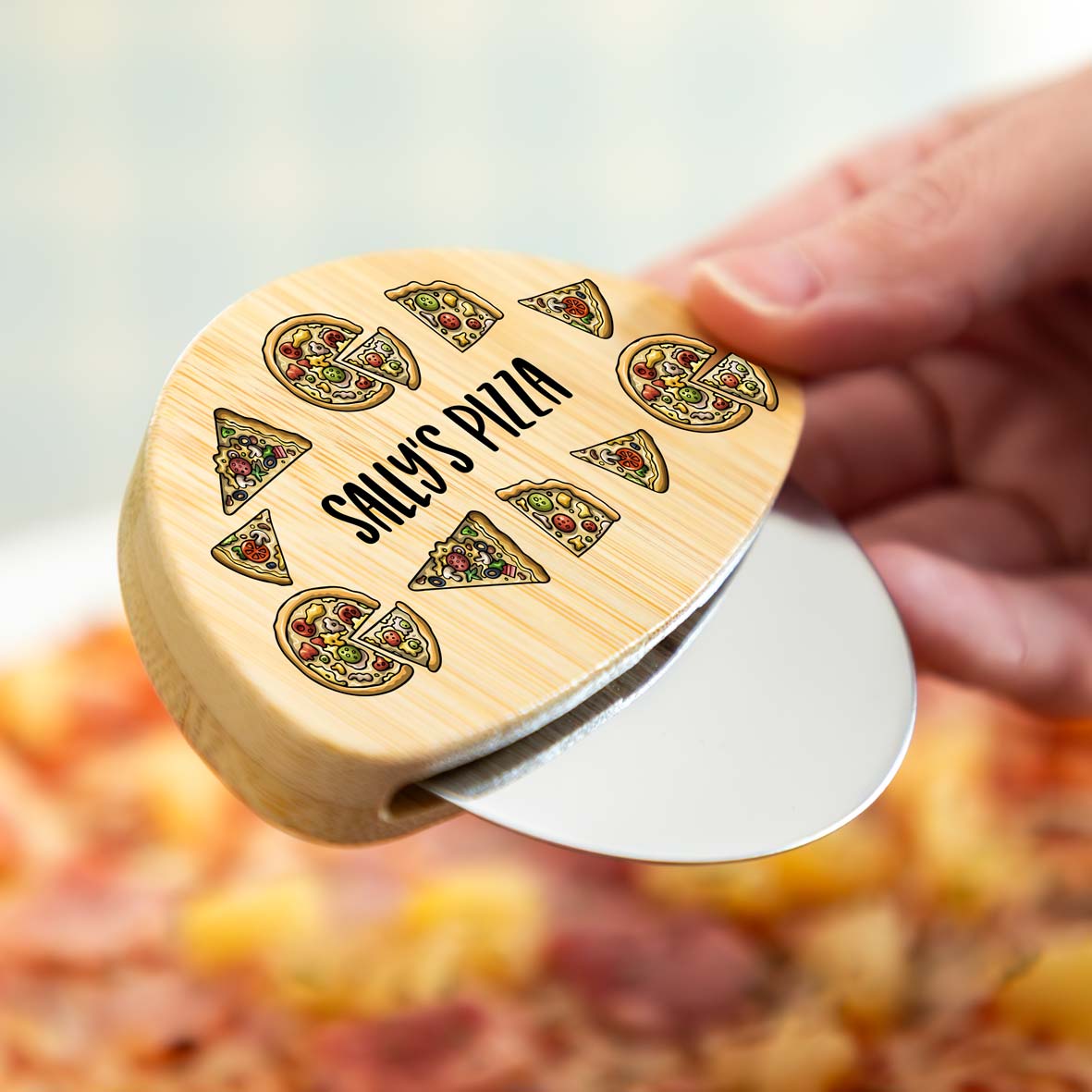 Person holding a wooden pizza cutter wheel with personalised text over a pizza.