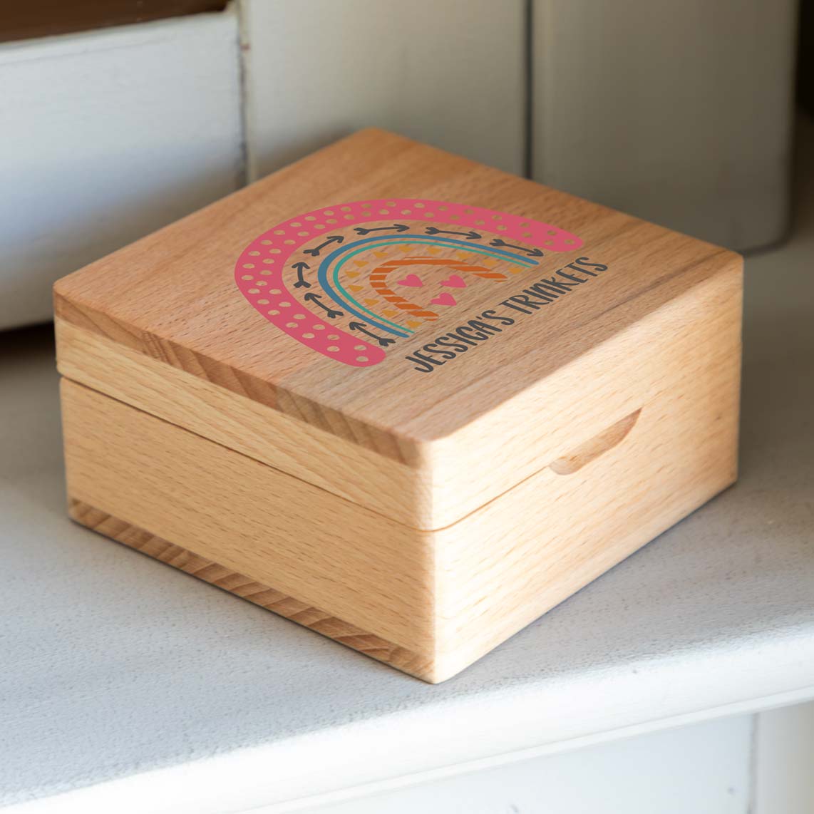 Closed wooden jewellery box on a white shelf, with a colourful rainbow and custom text printed on the lid.