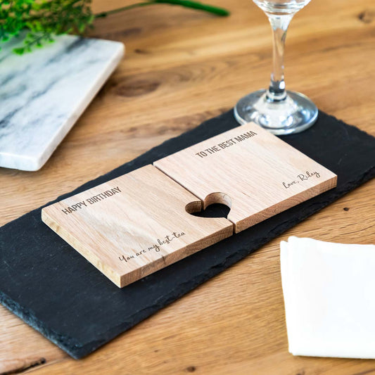 Personalised wooden coaster set with heart cutout on a wooden table with a glass and marble slab in the background.