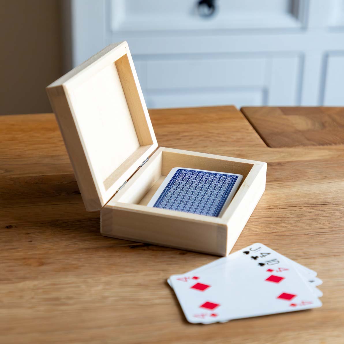 Wooden playing cards box open with playing cards on a wooden surface.