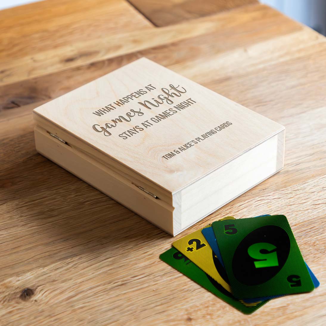 Wooden playing cards holder box with text on a wooden surface, featuring playing cards.