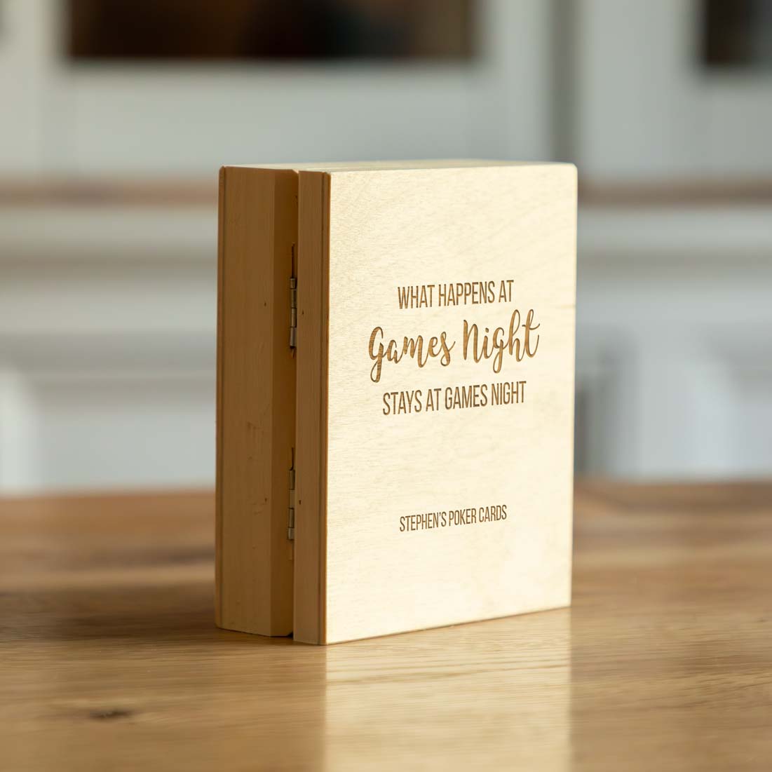 Wooden playing cards box with text 'What happens at games night stays at games night' on a wooden surface.