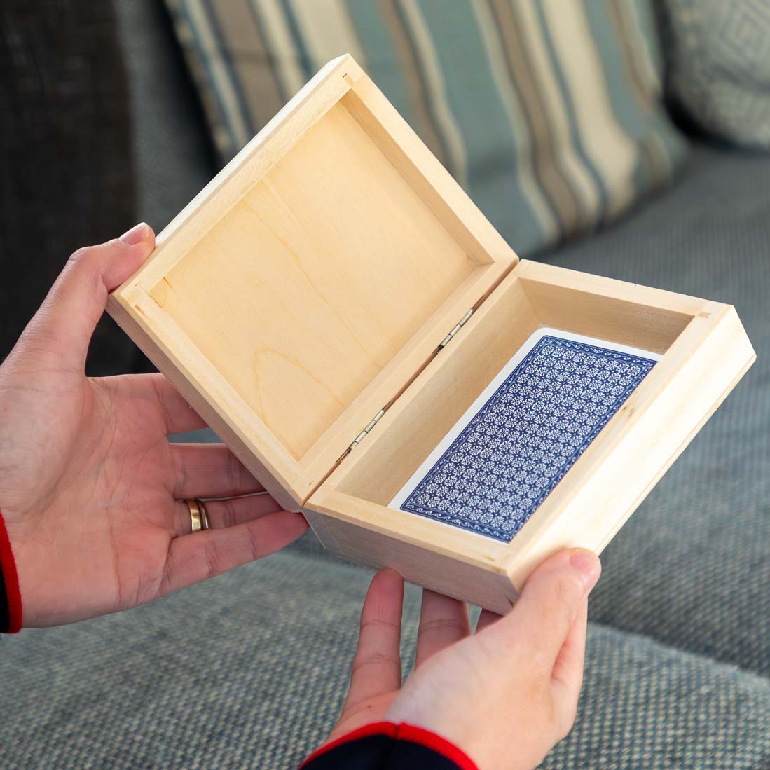A person holding a small wooden playing cards holder box with playing cards inside.