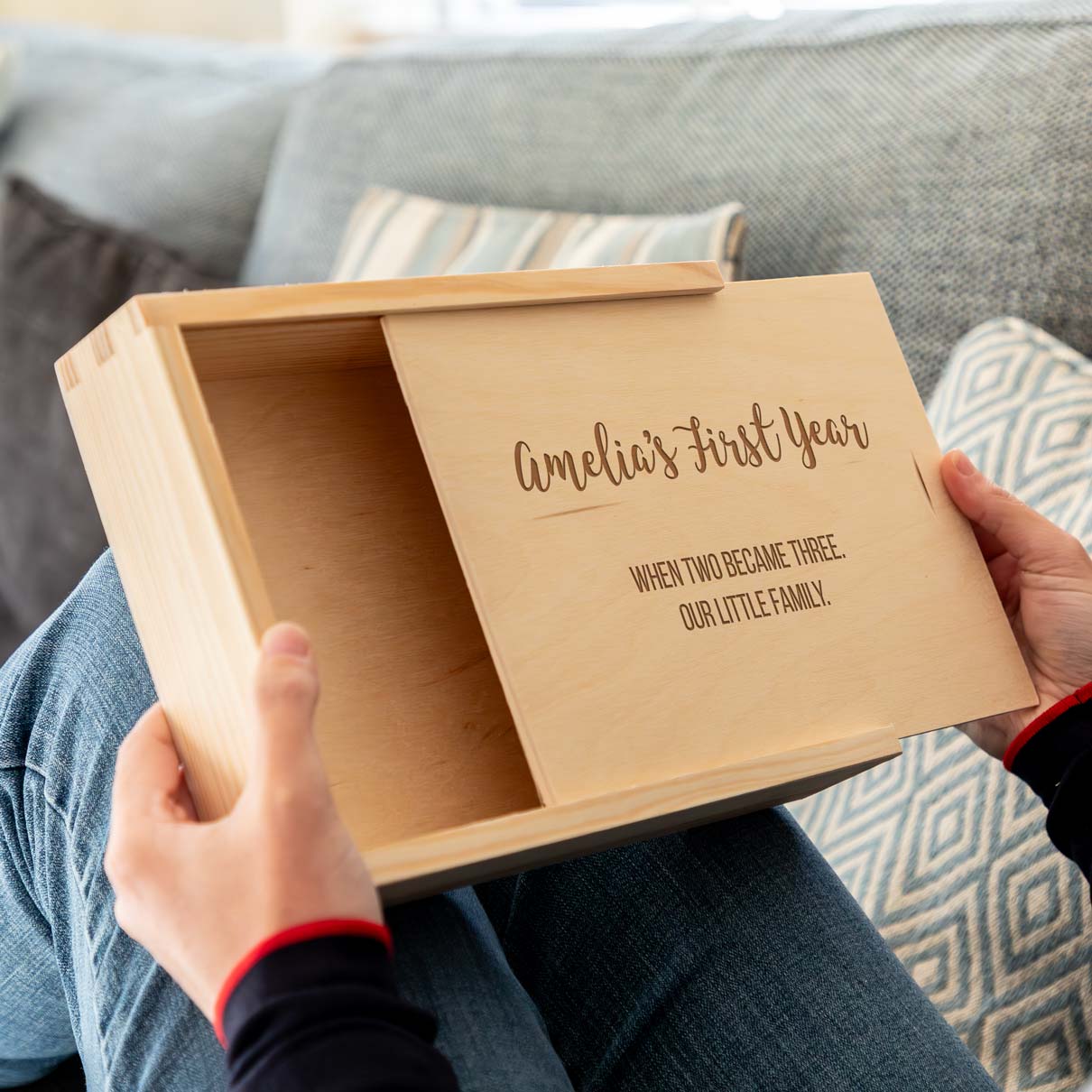 Wooden photo box with sliding lid, engraved with personalised text to celebrate a new baby held by a person, sitting on a couch.