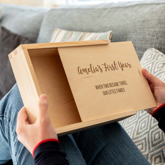 Wooden photo box with sliding lid, engraved with personalised text to celebrate a new baby held by a person, sitting on a couch.