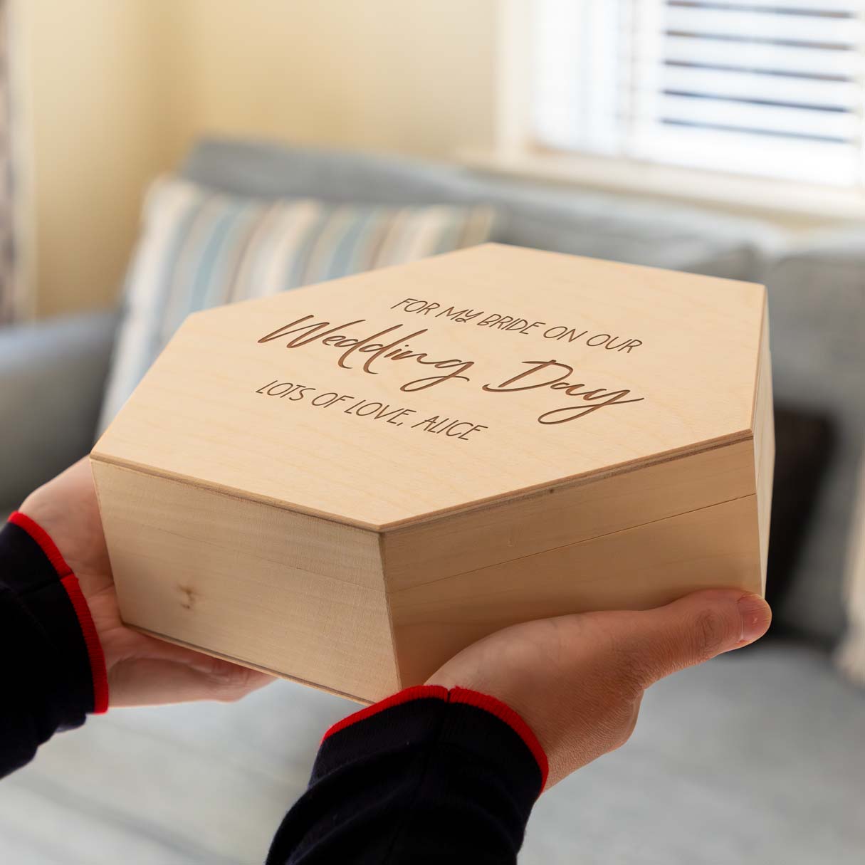Wooden hexagon keepsake box with engraved text held by a person in a living room setting