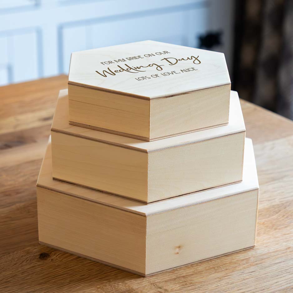 Stack of wooden hexagonal keepsake boxes with engraved text on a wooden surface.