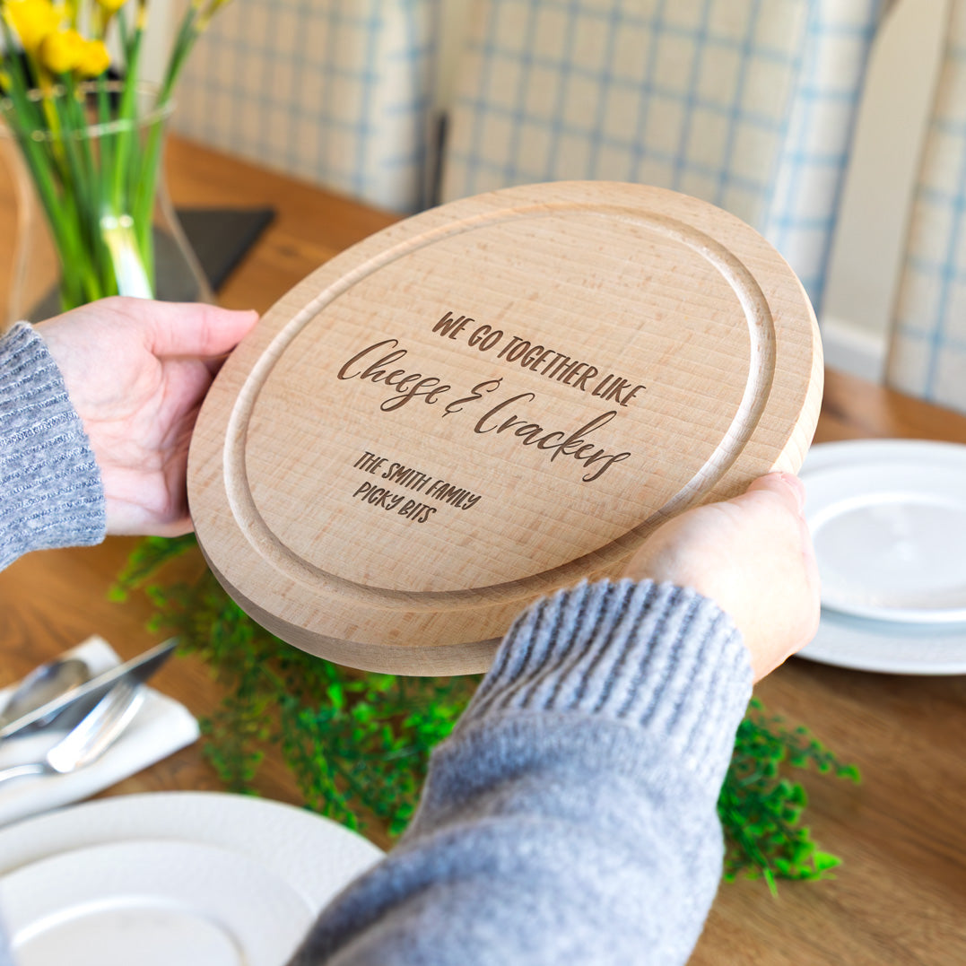 Person holding a wooden cheese board with engraved personalised text at a dining table.