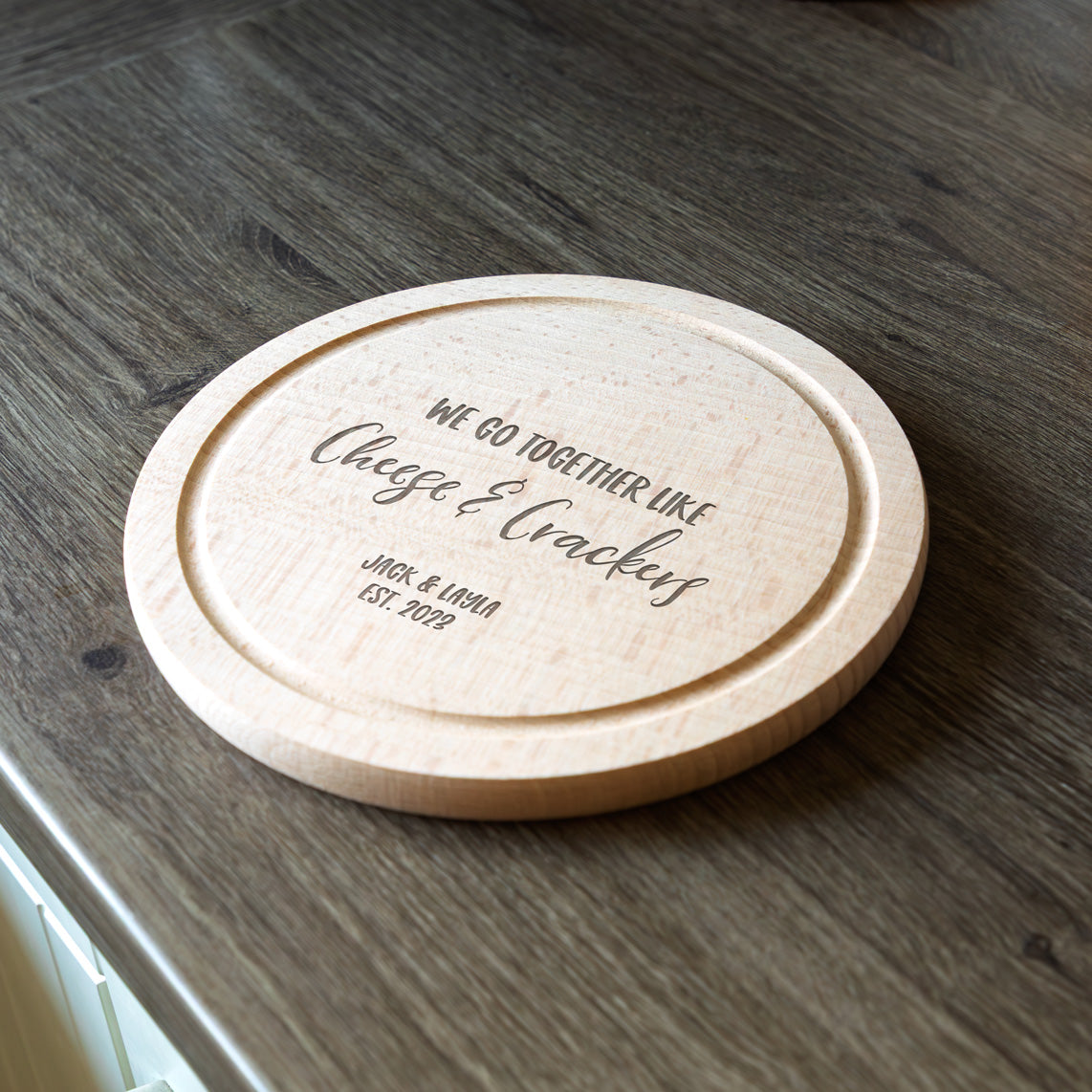 Round wooden cheese board with engraved personalised text on a wooden surface.