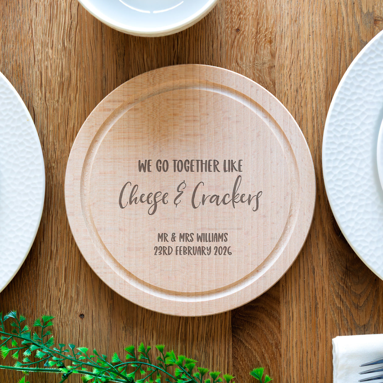 Wooden cheese board with engraved personalised text on a wooden table.