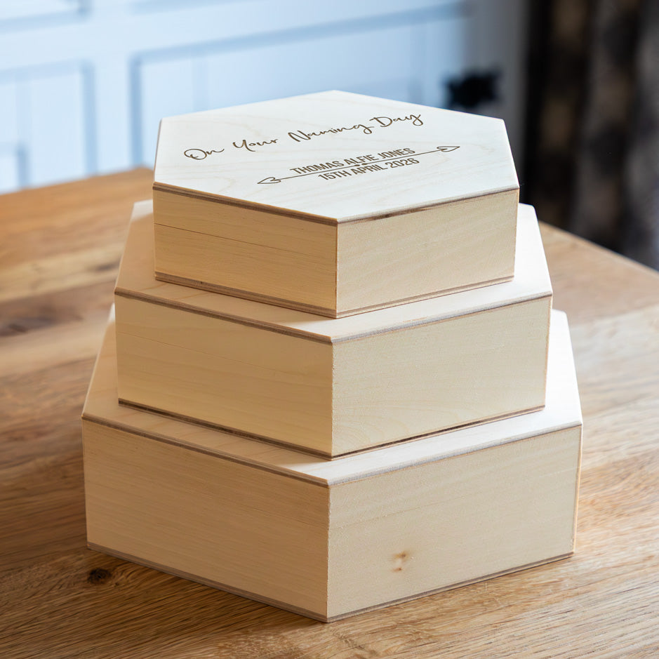 Stack of hexagonal wooden keepsake boxes with engraved text 'On Your Naming Day'.