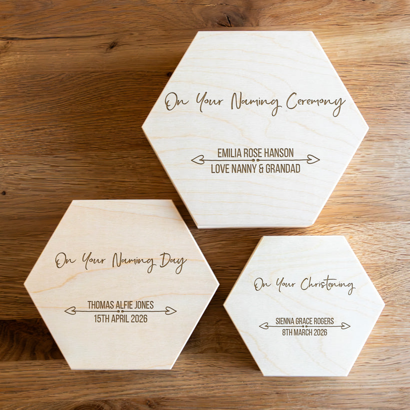 Three hexagonal wooden keepsake boxes in small, medium and large with engraved personalised text on a wooden surface.