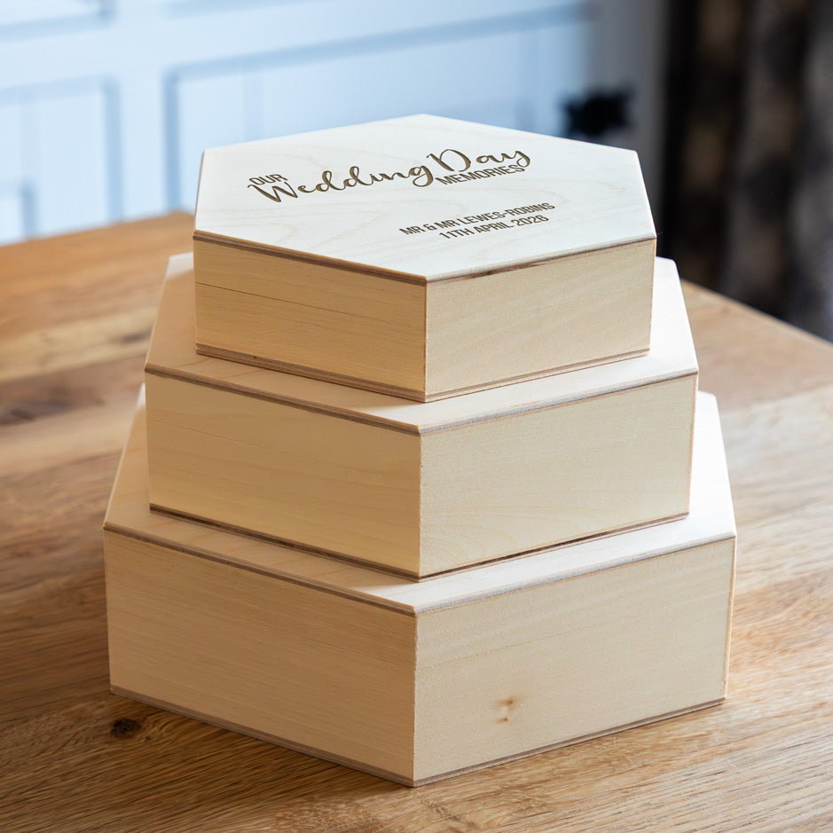 Stack of wooden hexagonal keepsake boxes with engraved text on a wooden surface.