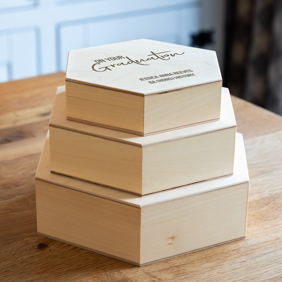 Stack of wooden hexagon keepsake boxes with engraved personalised lids on a wooden surface.