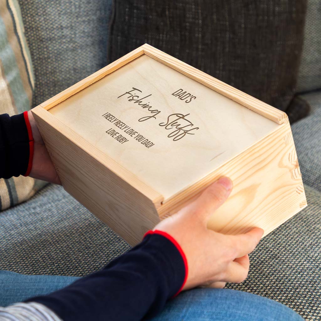 Wooden fishing box engraved with 'Dad's Fishing Stuff' held by a person on a couch.