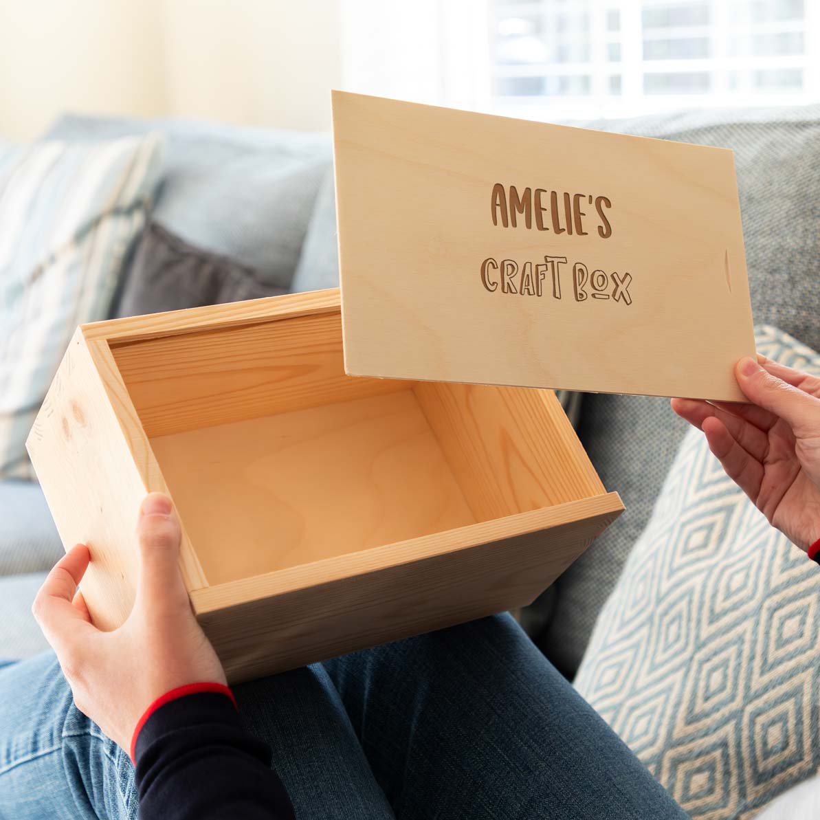 Wooden craft box with a sliding lid engraved with the personalised text, held by a person on a couch.