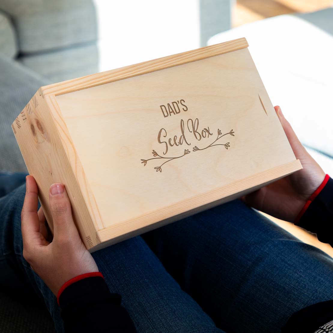 Wooden garden box engraved with 'Dad's Seed Box' held by a person.