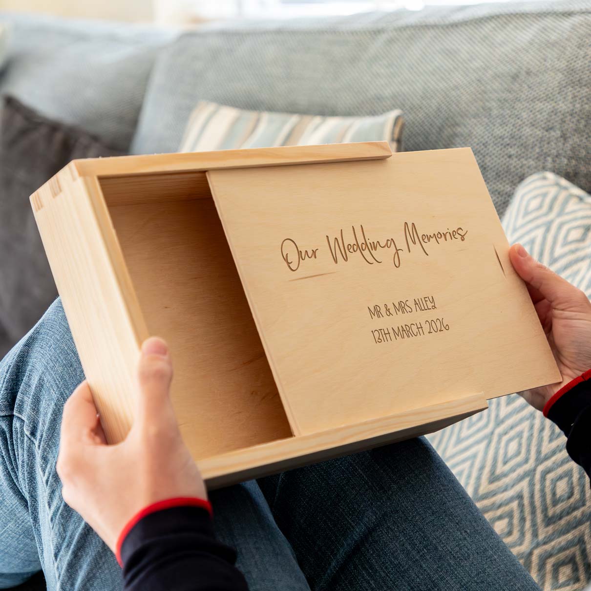 Wooden photo box with 'Our Wedding Memories' and personalised text engraving held by a person on a couch.