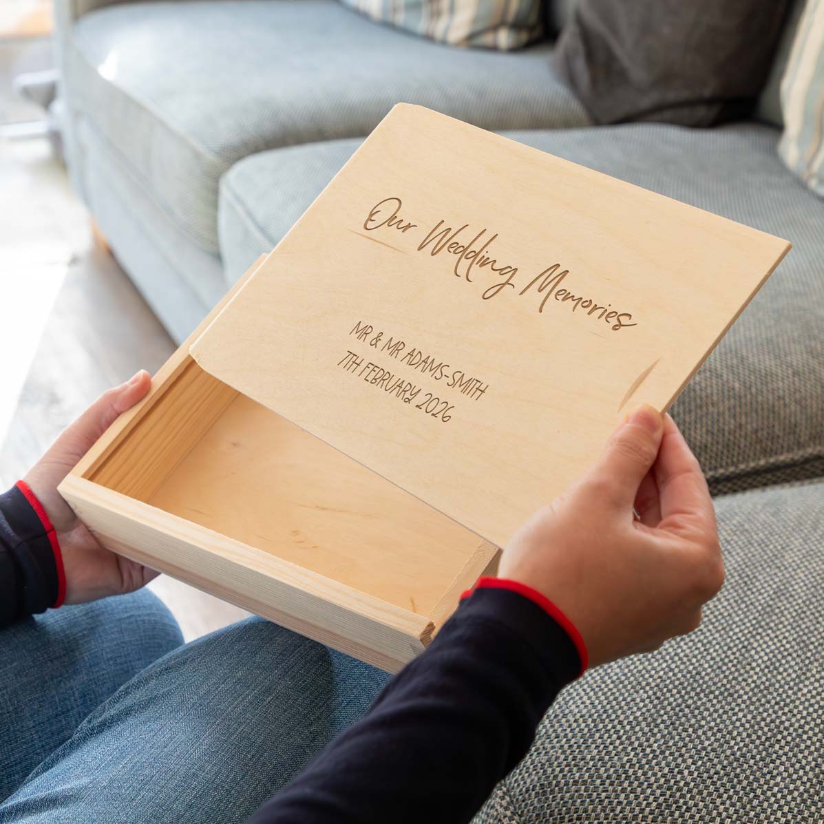 Wooden photo keepsake box engraved with 'Our Wedding Memories' and the personalised name and date, held by a person on a couch.