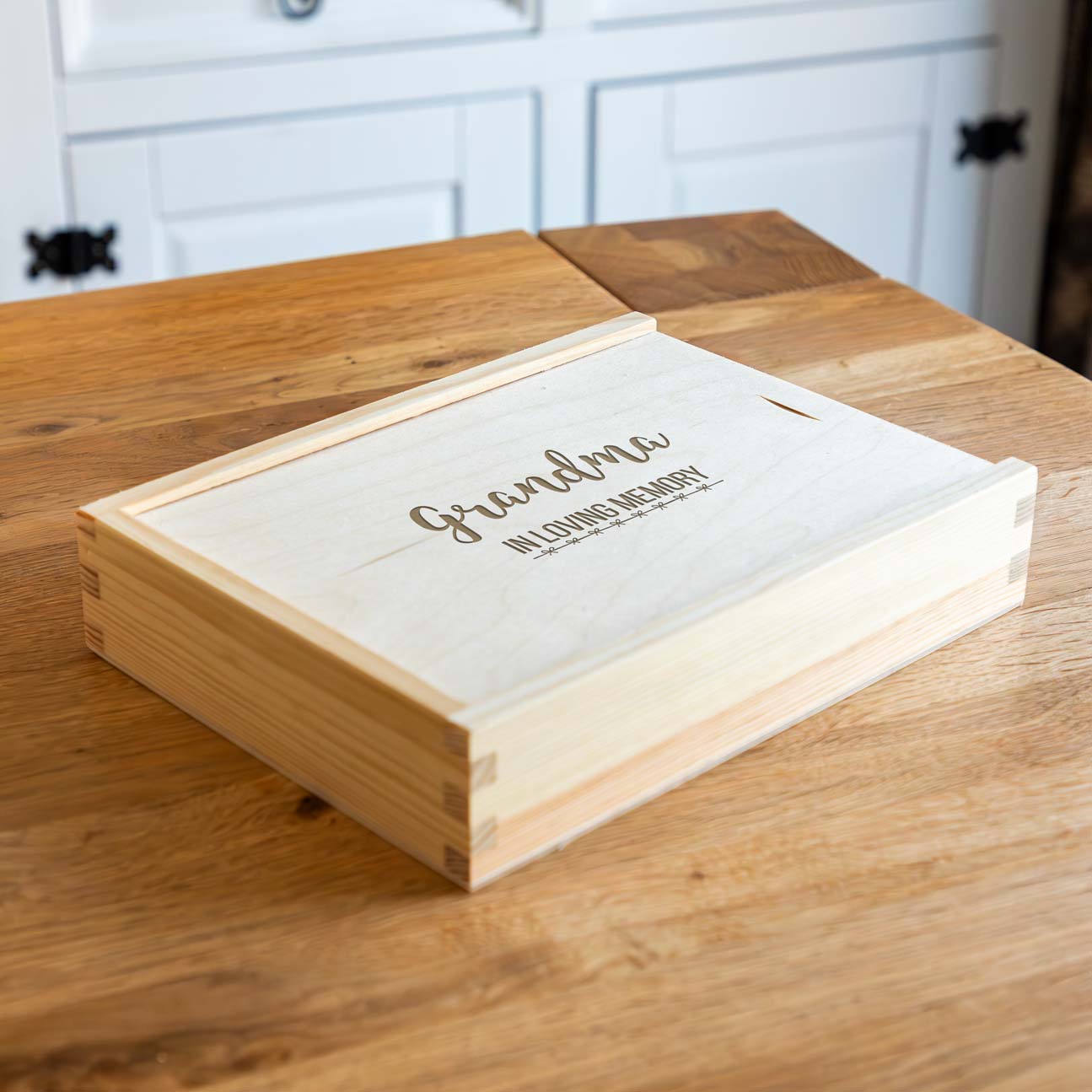 Wooden photo keepsake box with 'in loving memory' engraved on it, placed on a wooden surface.