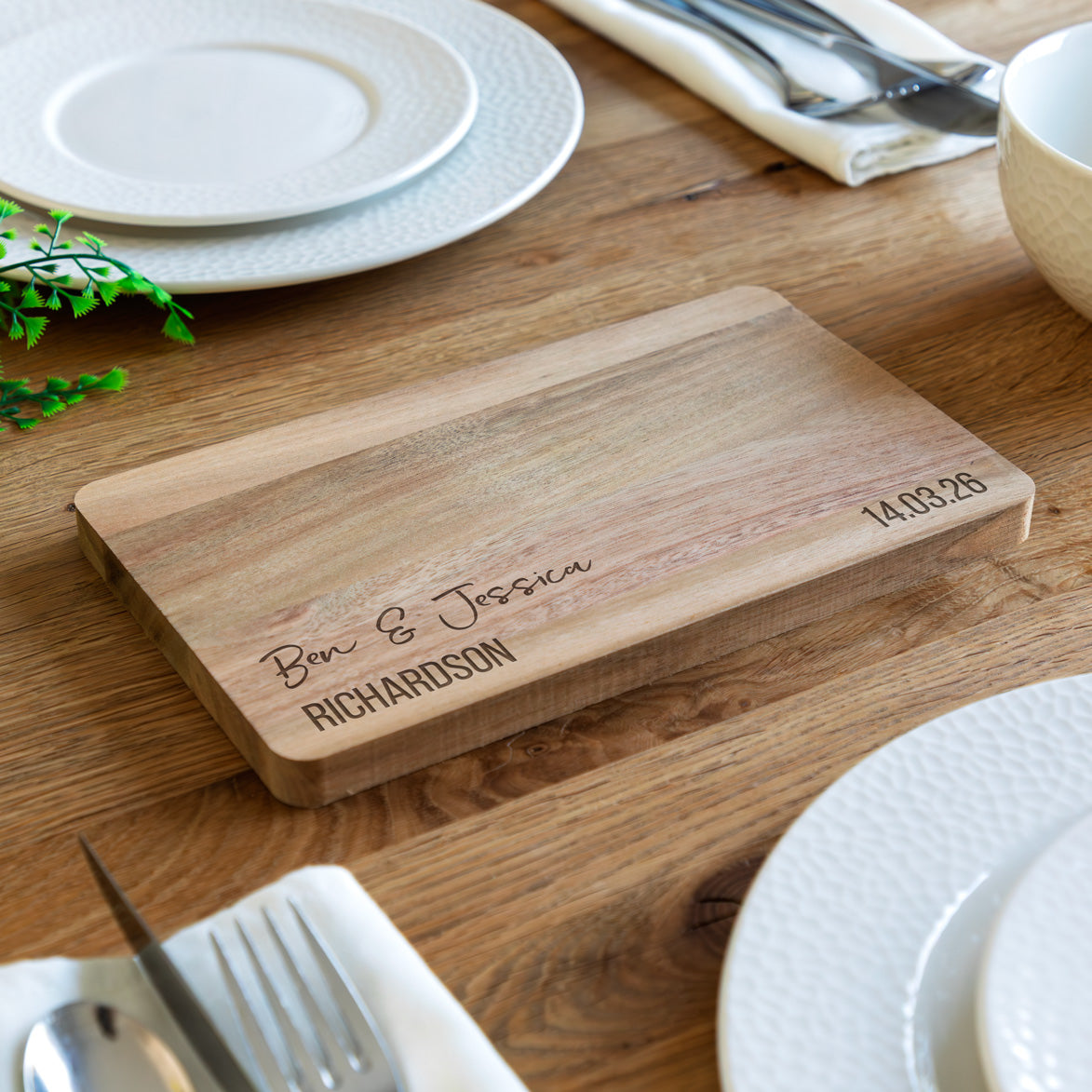 Wooden serving board with personalised engraved text on a wooden table with plates and cutlery.
