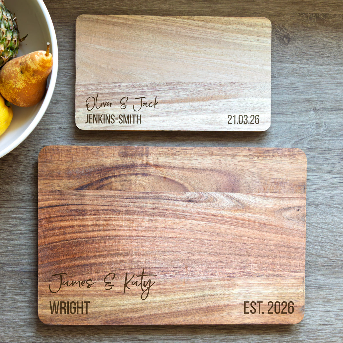 Two wooden serving boards in small and large sizes with engraved personalised names and dates on a wooden surface.
