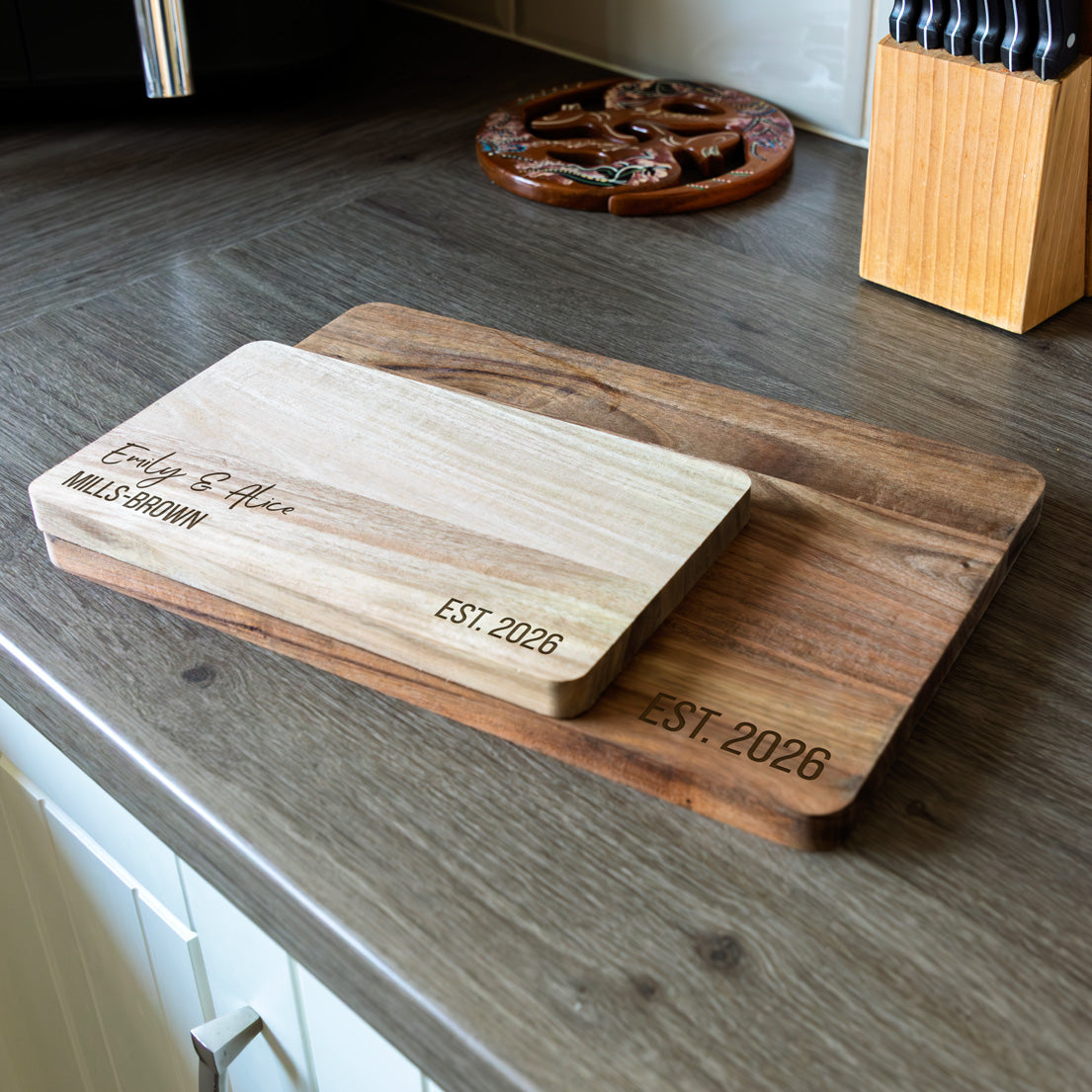 Two wooden serving boards with engraved personalised text on a kitchen counter.