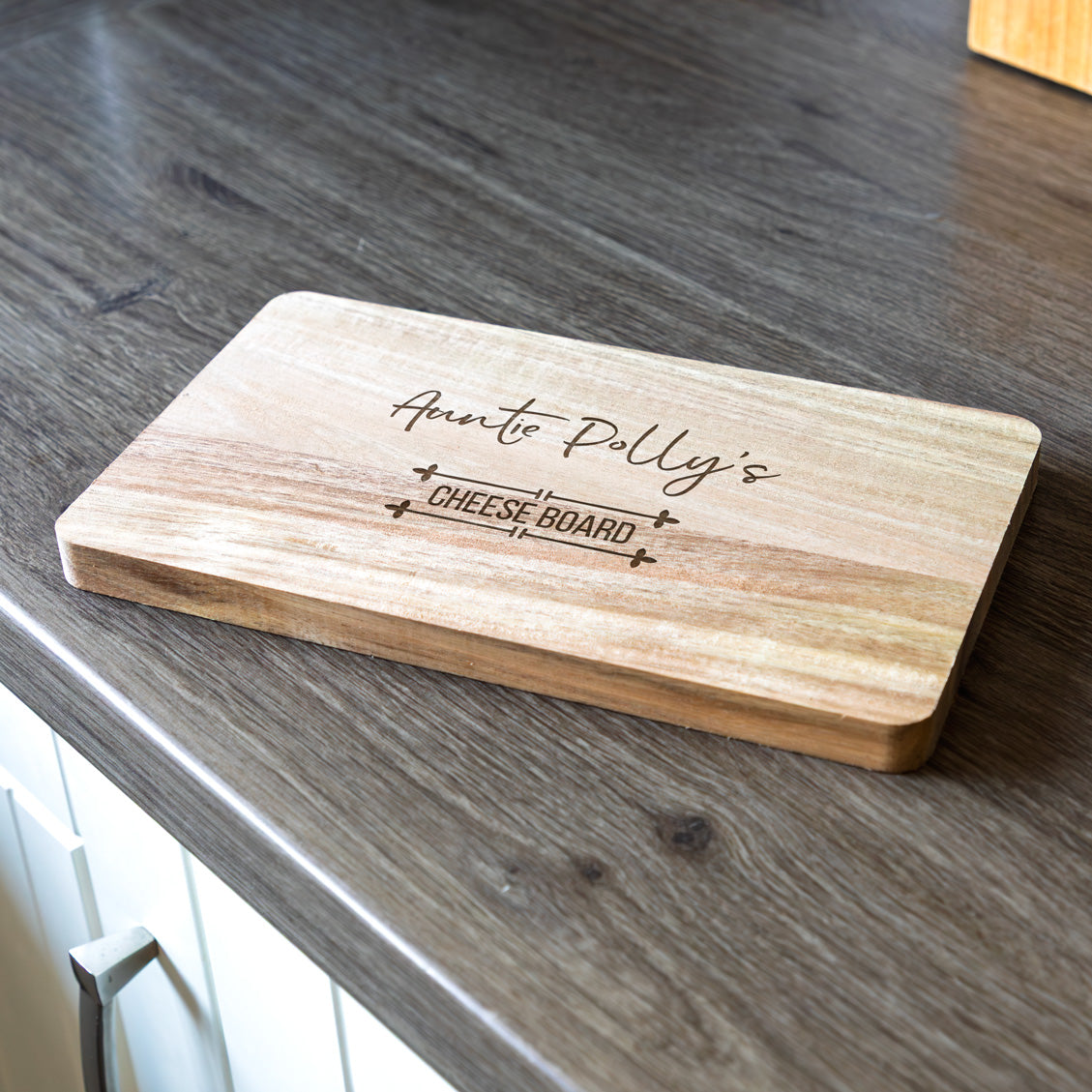 Wooden personalised cheese board with engraved text on a wooden surface.