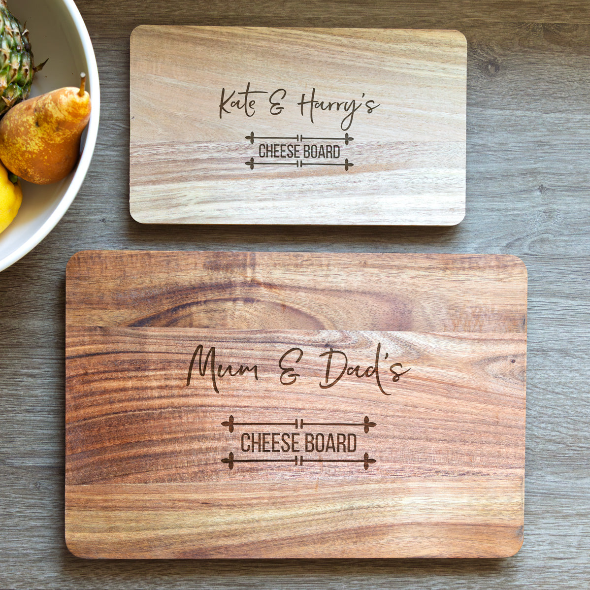 Two wooden cheese boards in small and large sizes, with engraved personalised text on a wooden surface.