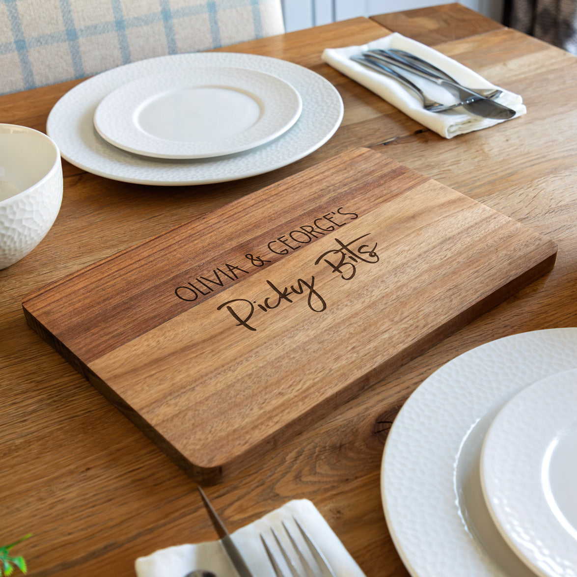 Wooden serving board for picky bits with engraved personalised text on a dining table with plates and cutlery.
