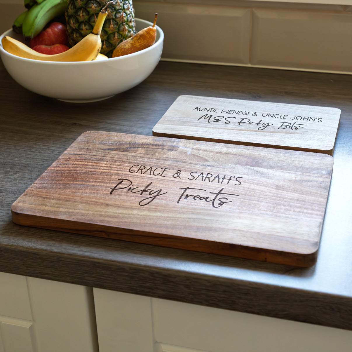Two wooden picky bits serving boards with engraved text on a kitchen counter.
