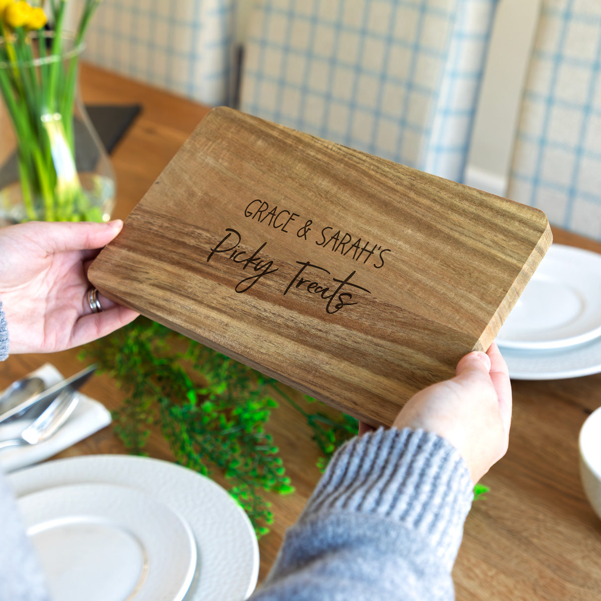 Wooden picky bits serving board with engraved personalised text held by a person on a dining table.
