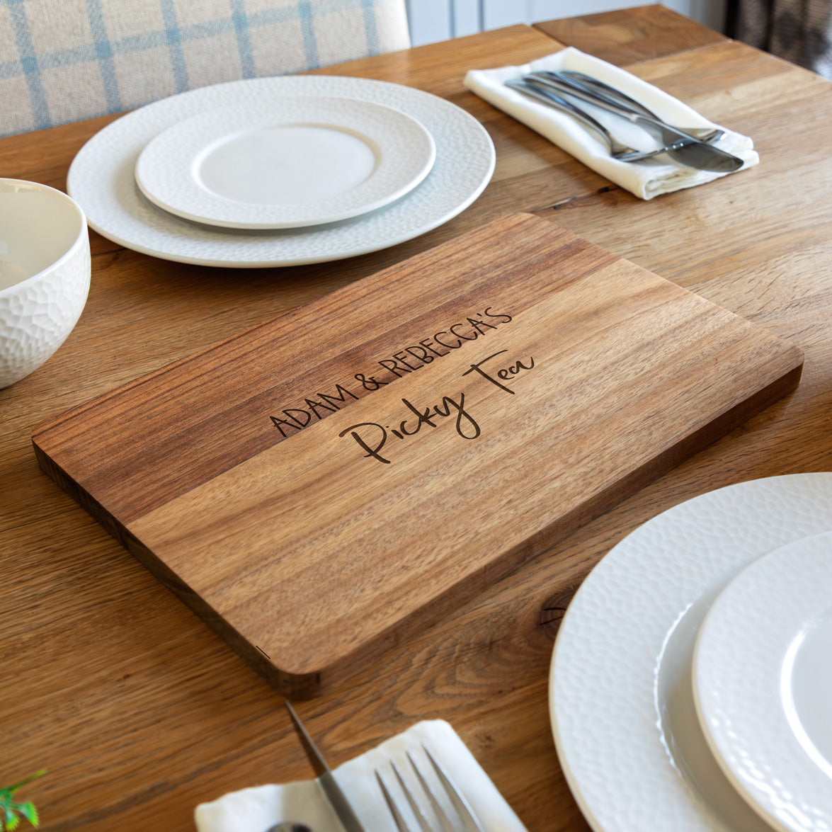 Wooden serving board for 'picky tea' with engraved personalised  text on a dining table with plates and cutlery.