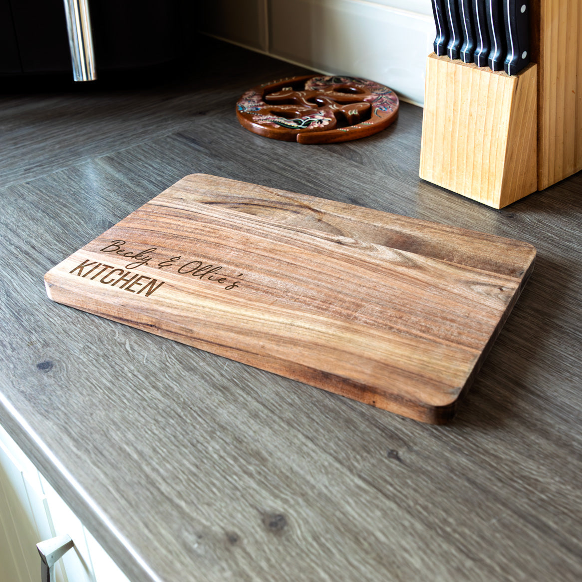 Wooden chopping or serving board with engraved personalised text on a kitchen worktop.
