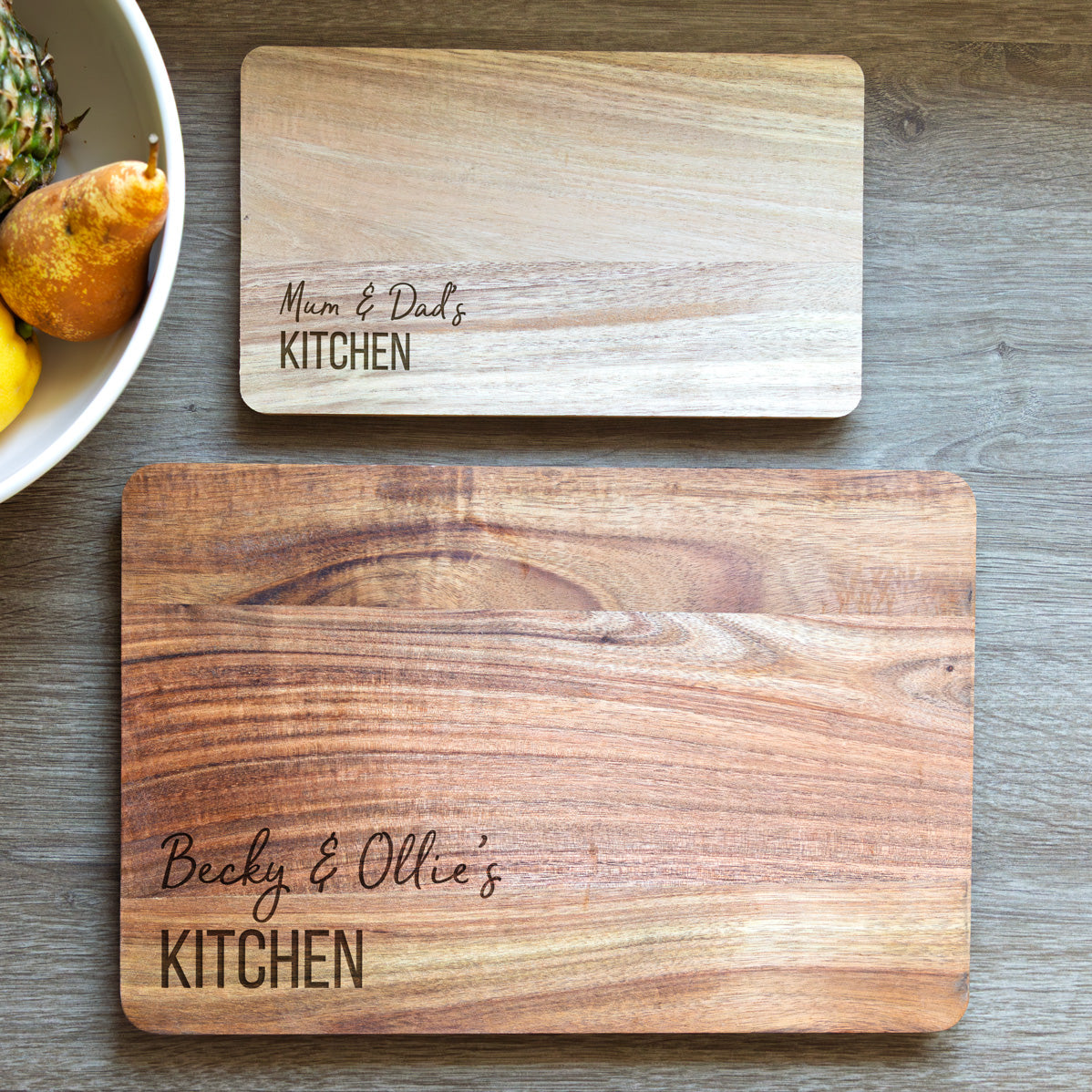 Two wooden cutting boards with engraved personalised names on a wooden surface.