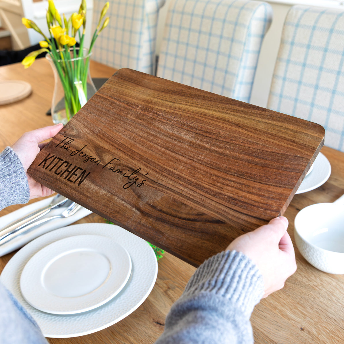 Wooden cutting board with engraved personalised text held by a person on a dining table.