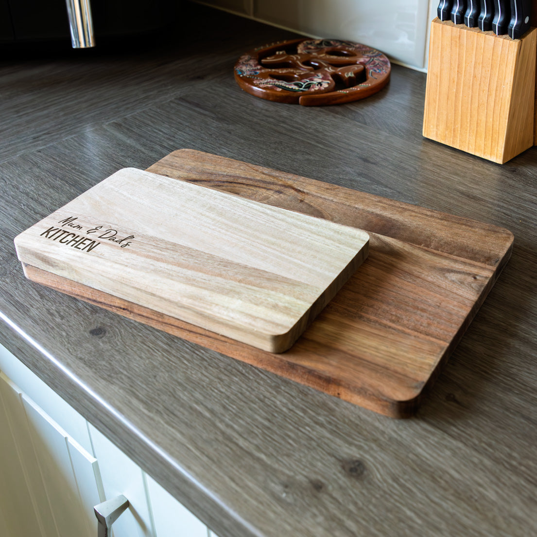 Two wooden cutting boards with engraved personalised text on a kitchen counter.