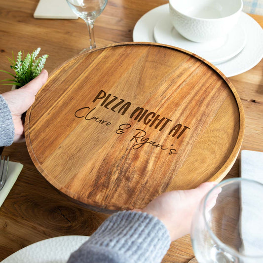 Wooden pizza board engraved with 'Pizza Night at' text and the personalised names, on a dining table.
