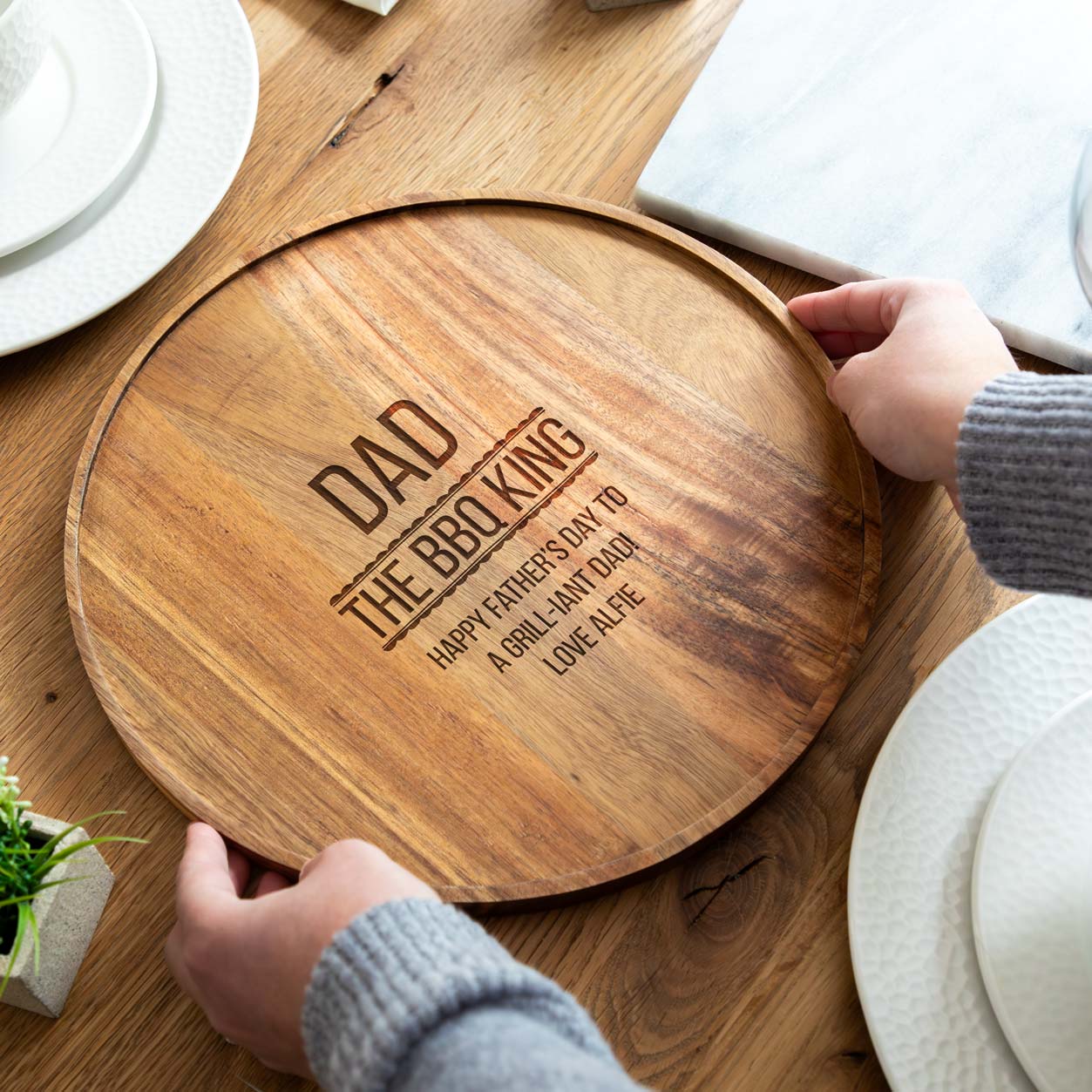 Wooden serving board engraved with 'The BBQ King' and a personalised name and message, on a dining table.