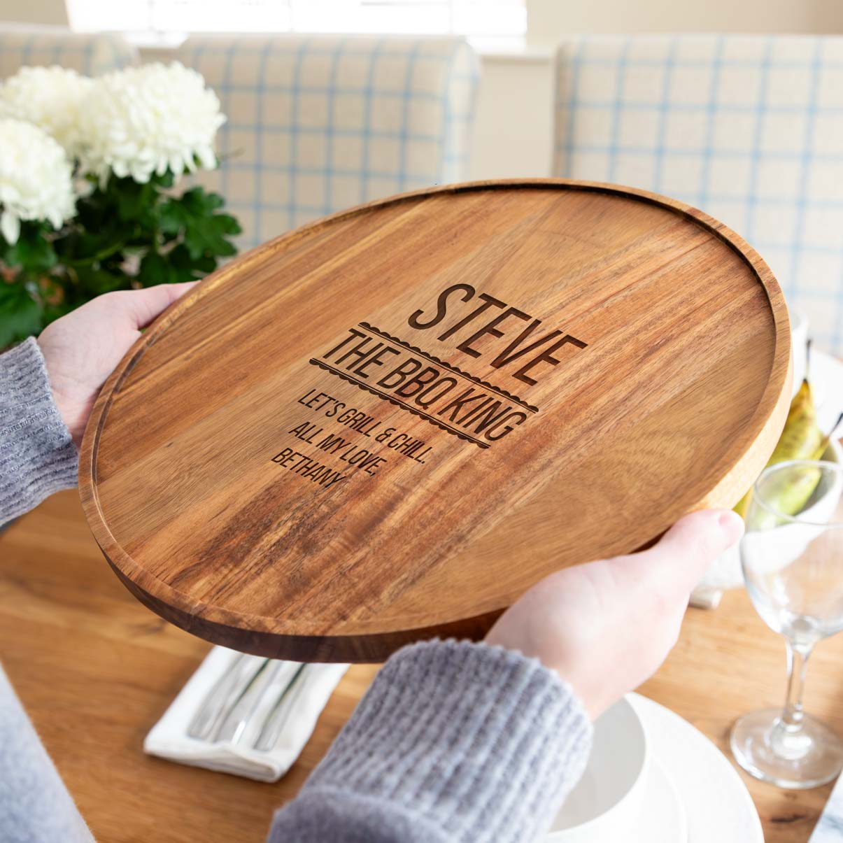 A person holding an acacia wood serving board engraved with 'The BBQ King' text and a personalised name and message.