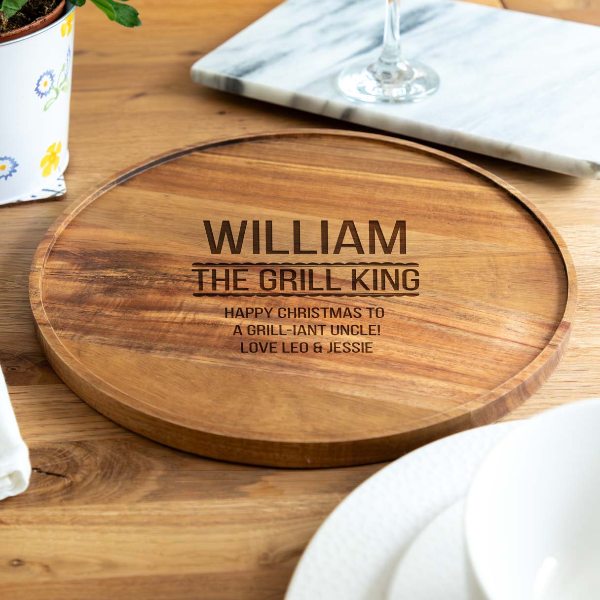 Wooden serving board engraved with 'The Grill King' text and a personalised name and message, on a wooden table.