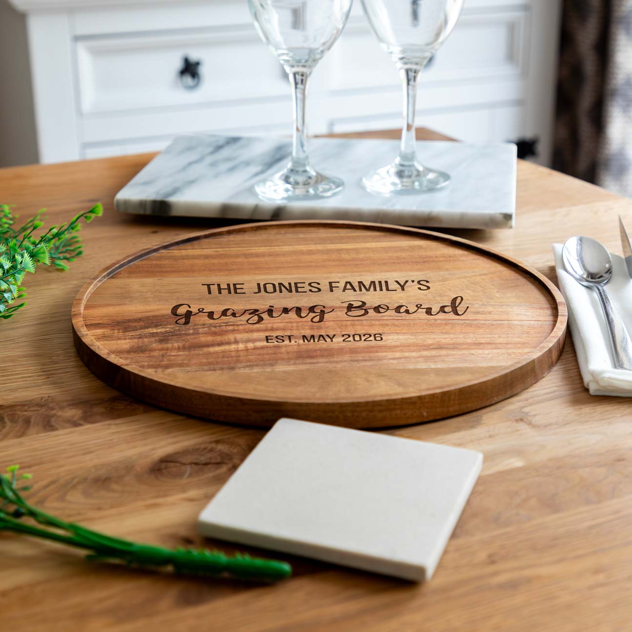 Wooden grazing board with engraved text on a dining table with wine glasses and cutlery.