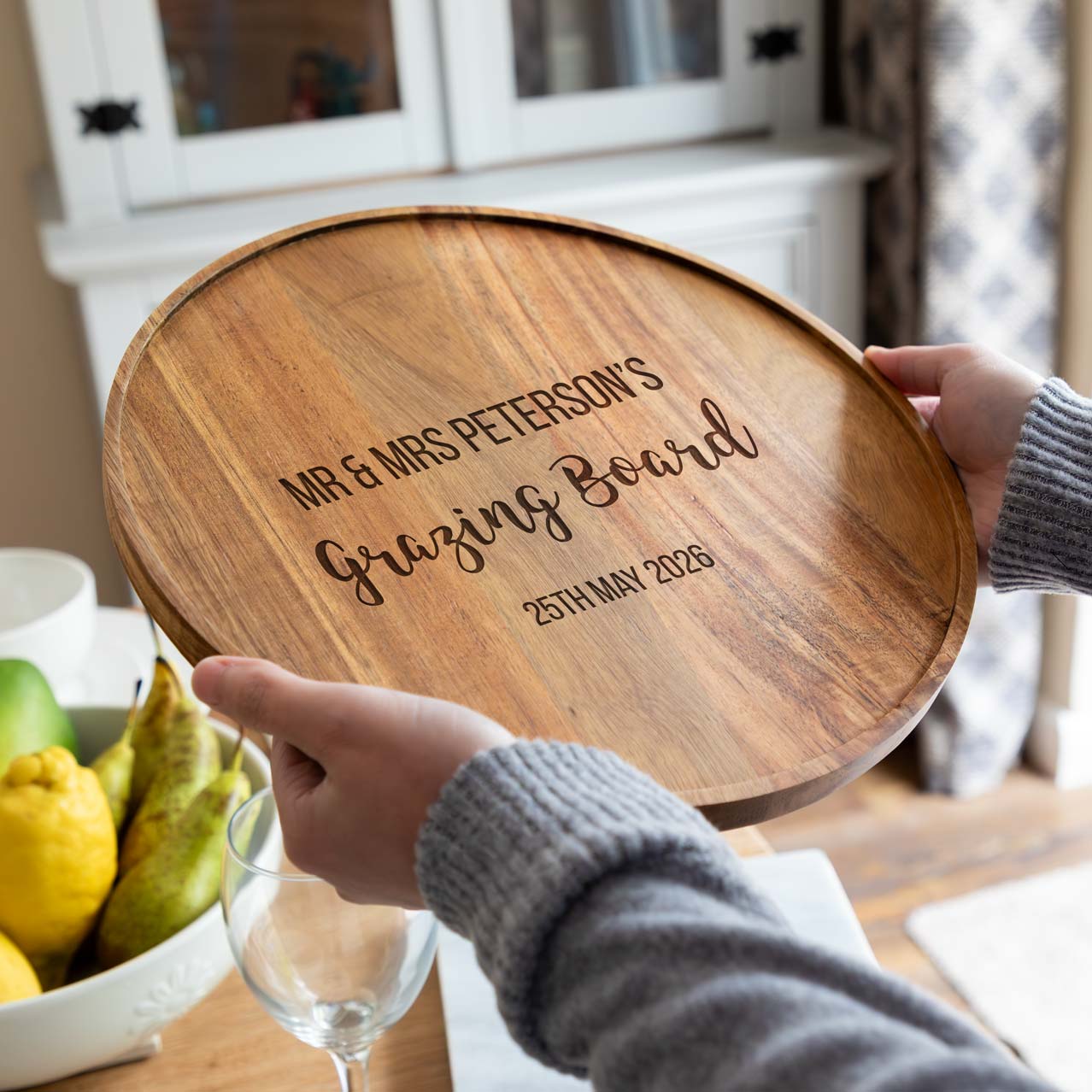 A person holding a wooden grazing board with engraved text, personalised with a married name and wedding date.
