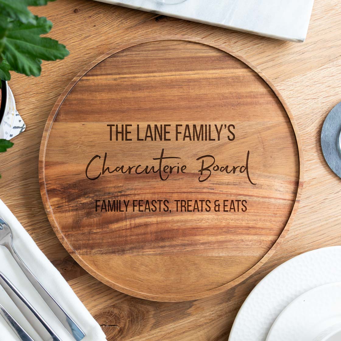 Wooden personalised charcuterie board with engraved text on a wooden surface.