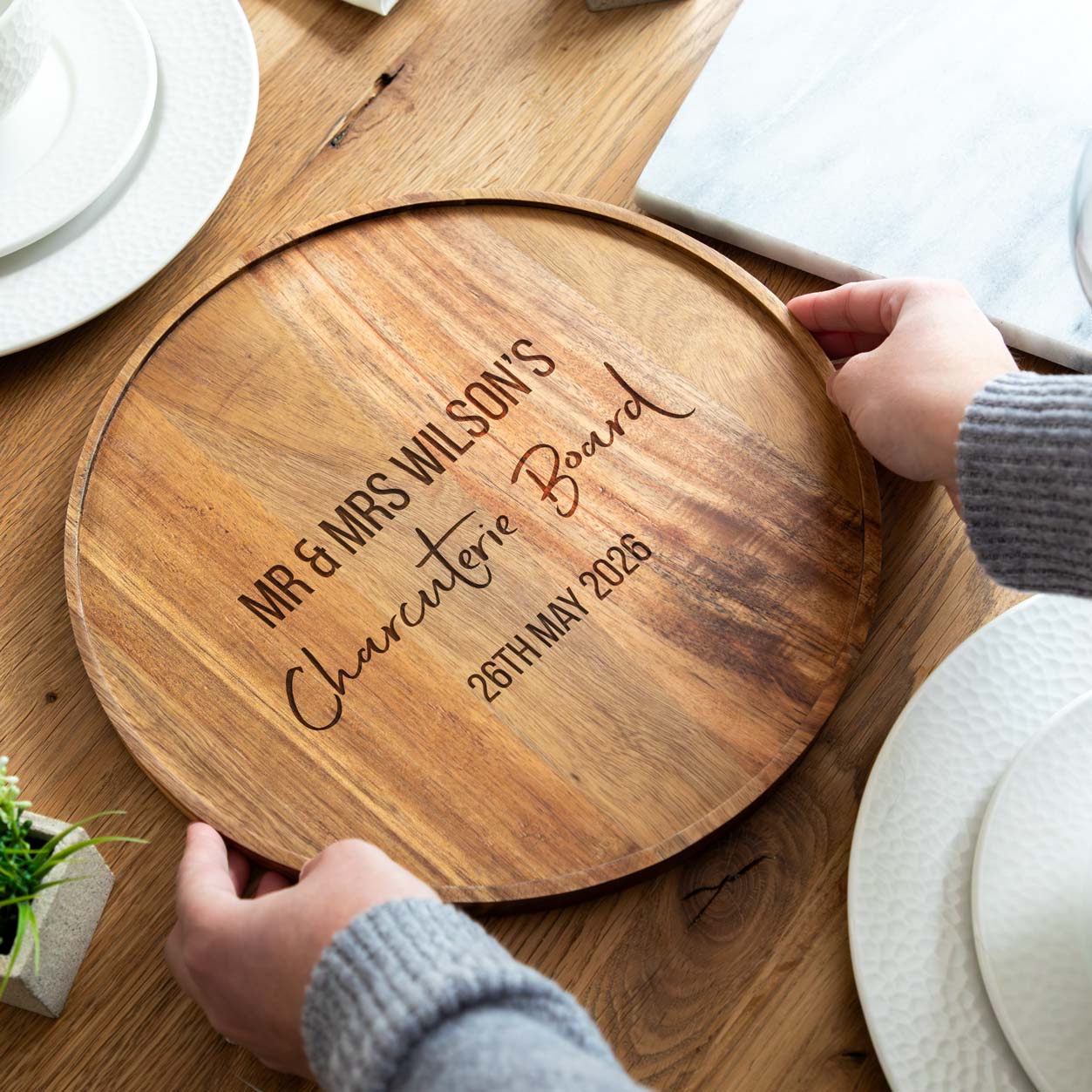 Wooden charcuterie board with engraved text on a wooden table, personalised with a married name and wedding date.