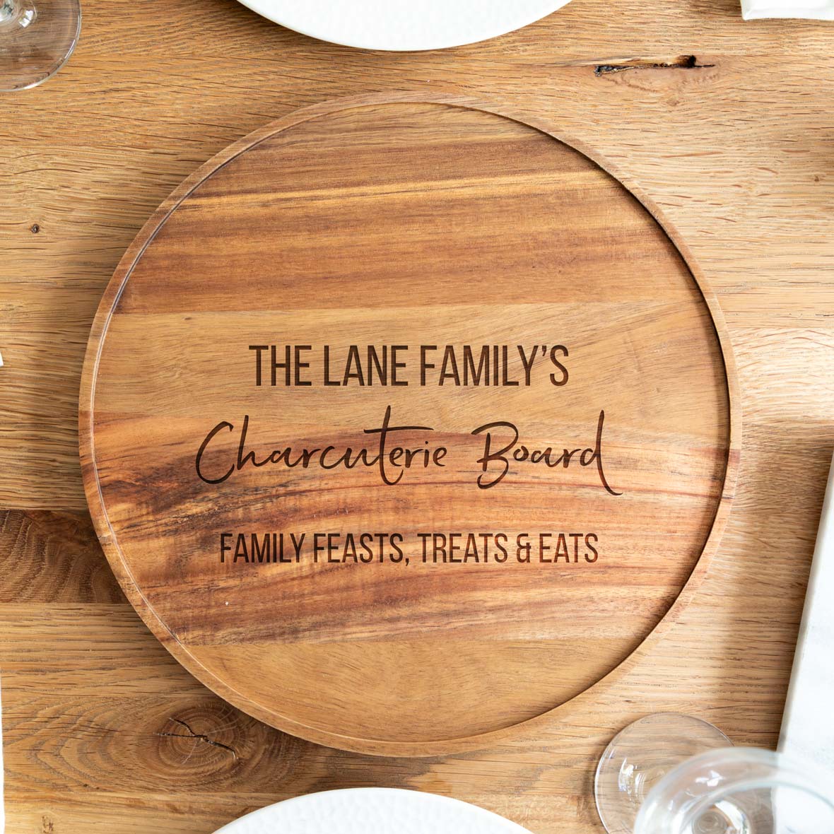 Wooden personalised charcuterie board with engraved text on a wooden surface.